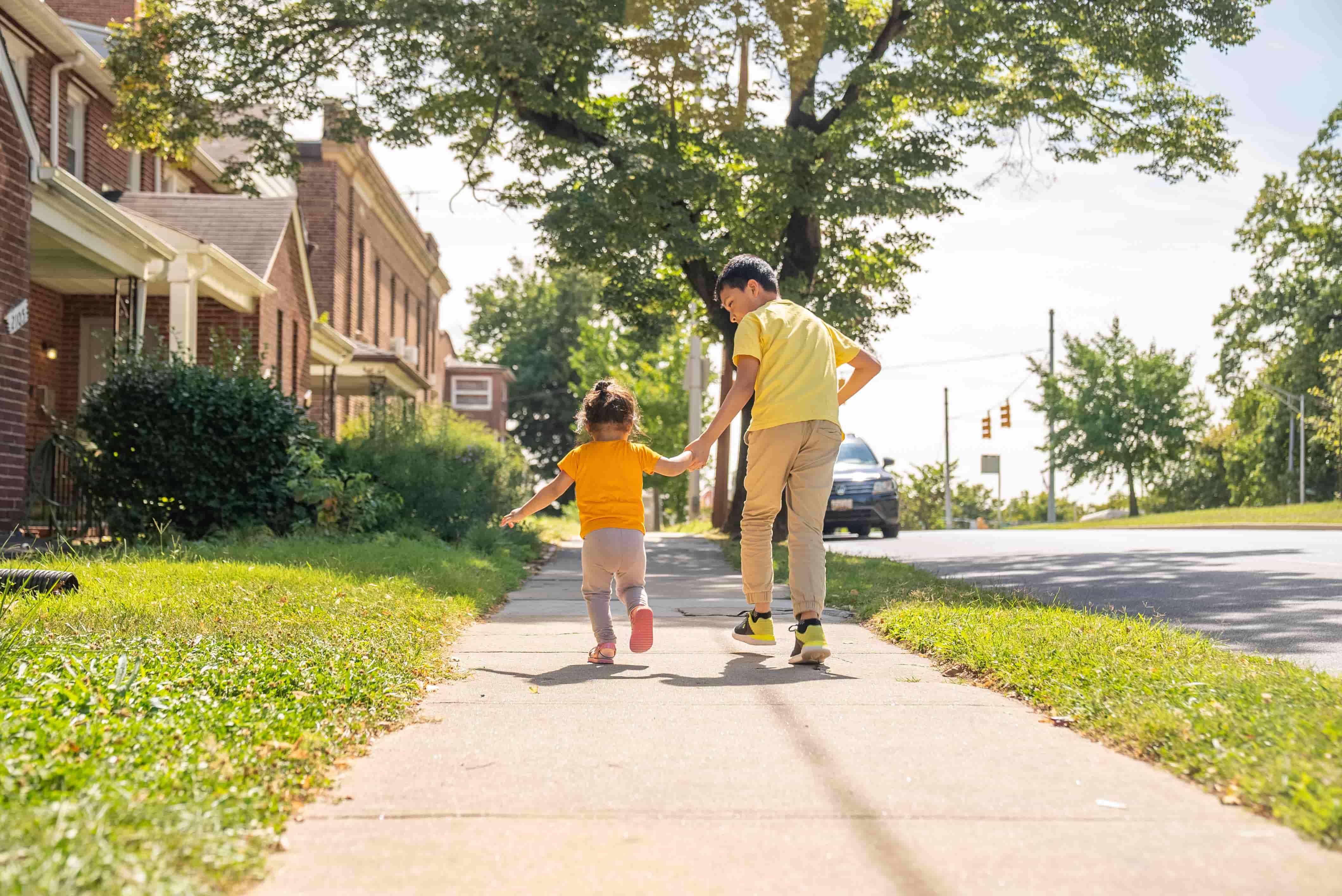A boy and a young girl holding hands running down a sidewalk